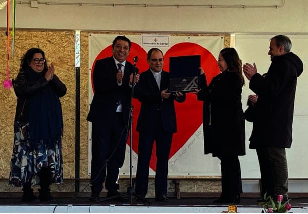Cinco pessoas num palco, diante de um grande coração vermelho, numa cerimónia de entrega de uma placa