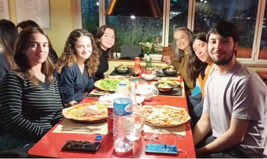 Jovens e adultos sentados à volta de uma mesa de restaurante, a sorrir para a câmara