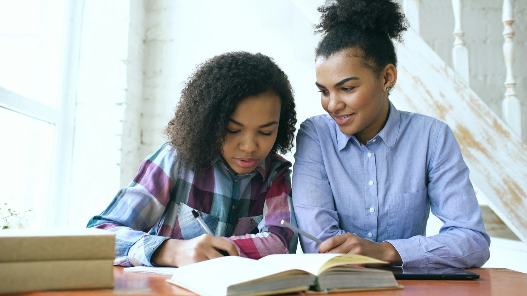 Duas jovens a estudar juntas a uma mesa, com um livro aberto